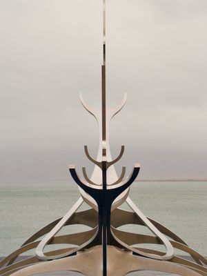 A symmetrical view of Sun Voyager, a famous art installation of a stylized viking ship made of stainless steel in Reykjavík, Iceland. The ocean and an overcast sky can be seen in the background.