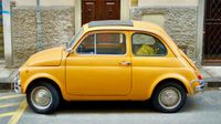 Side view of a small yellow car parked by the sidewalk on a quiet street in Florence.