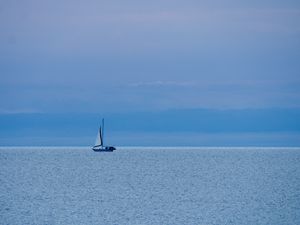 Many shades of blue from the sky and water meet in the middle of the photo where a small sailboat sits on the horizon.