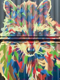 An orthogonal view of a raccoon's face painted on the side of a shipping container using hundreds of technicolor polygons.