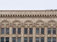 An orthogonal view of the top floors of an old building with intricately decorated windows and stonework.