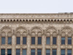 An orthogonal view of the top floors of an old building with intricately decorated windows and stonework.