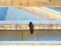 Looking down at a woman standing alone and leaning against the wall of a pedestrian bridge. Other bridges at different levels can be seen in frame at interesting angles.