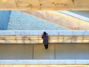 Looking down at a woman standing alone and leaning against the wall of a pedestrian bridge. Other bridges at different levels can be seen in frame at interesting angles.