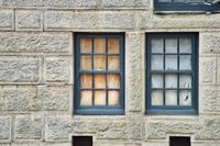 An othogonal view of two windows in an old stone wall. They're off-center and papered over from the inside with brown and white paper.