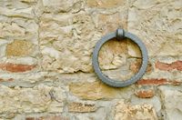 An orthogonal view of an old stone wall with a single metal ring hanging from a bolt.
