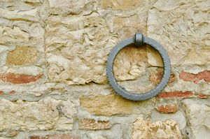 An orthogonal view of an old stone wall with a single metal ring hanging from a bolt.