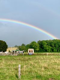 A rusty, abandoned truck in a farmer's field is framed overhead by a wide, crisp rainbow.