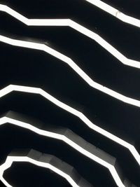 Abstract view of white lights on a black ceiling. The lights are long and continuous in the form of topographic lines on a map resulting in a stripe effect.