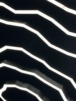 Abstract view of white lights on a black ceiling. The lights are long and continuous in the form of topographic lines on a map resulting in a stripe effect.
