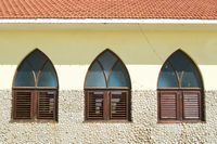 An orthogonal view of a bright yellow wall with three evently spaced arched windows framed in wood.