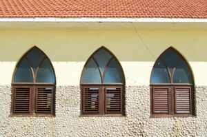 An orthogonal view of a bright yellow wall with three evently spaced arched windows framed in wood.