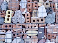An orthogonal mosaic of old eroded bricks and stones stacked behind a wire mesh.