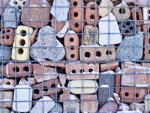 An orthogonal mosaic of old eroded bricks and stones stacked behind a wire mesh.