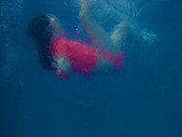 Underwater side profile of a young girl playfully sinking to the bottom of a pool.