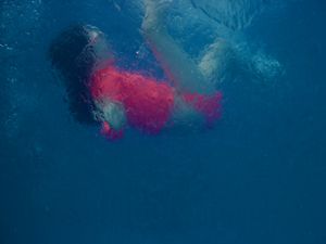 Underwater side profile of a young girl playfully sinking to the bottom of a pool.