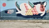 Back alley graffiti depicting a stylized naked woman wrestling a bird-like creature on an abstract basketball court.