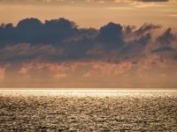 A dark cloud bank hides the sun while it makes the water sparkle in a golden light.