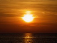 As the sun sets over Lake Huron the water is dark and the clouds are blazing orange.