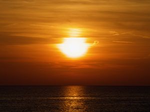 As the sun sets over Lake Huron the water is dark and the clouds are blazing orange.