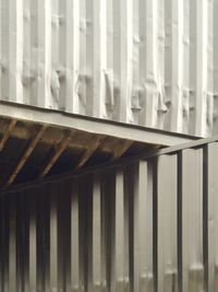 Looking up at 2 black shipping containers. The upper container is at an angle to the lower one and overhangs such that the underside forms a triangular shape in the center of the frame.