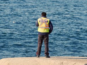 A security guard's back (and bright saftey vest) is to the camera as he watches the ocean which fills the entire background of the photo.