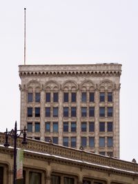 A distant view of an ornate old stone mid-rise building, with another stone building angled in the foreground. Both buildings feature many accents, carvings, and animal figures.