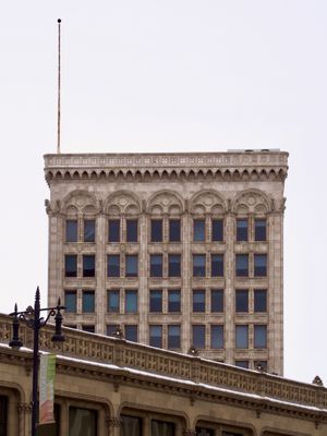 A distant view of an ornate old stone mid-rise building, with another stone building angled in the foreground. Both buildings feature many accents, carvings, and animal figures.