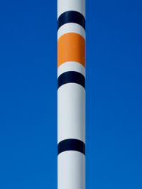 The top of a large fishing bobber in an outdoor art installation forms white, orange, and black stripes against a bright and sunny blue sky.