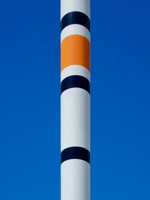 The top of a large fishing bobber in an outdoor art installation forms white, orange, and black stripes against a bright and sunny blue sky.