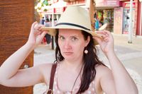 A head-and-shoulders portait of a beautiful woman staring mischievously at the camera while adjust a fedora on her head.