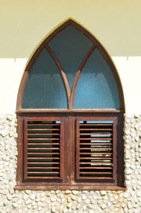 An orthogonal view of an arched window framed in wood and surrounded by plaster and stone.