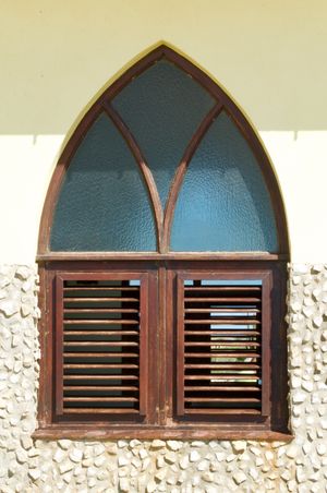 An orthogonal view of an arched window framed in wood and surrounded by plaster and stone.