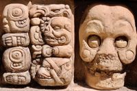 Close-up of Mayan glyphs carved in stone predominantly featuring skulls and animals.