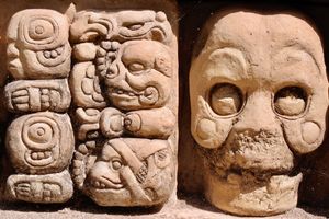 Close-up of Mayan glyphs carved in stone predominantly featuring skulls and animals.