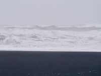 Looking at the ocean on a very foggy day. The photo is framed in three equal segments—the sky is light grey, the water is grey and white, and the ground is black volcanic sand.