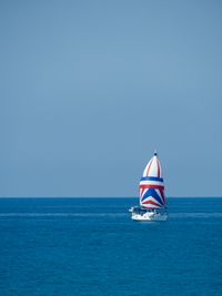 A sailboat crosses Lake Huron on a sunny day. The sail is white with red and blue stripes.