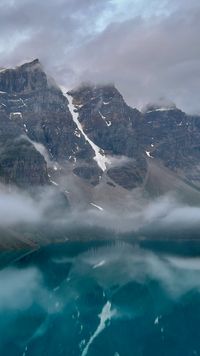 The snowy mountain peaks stand tall above Moraine Lake's crystal blue water as numerous cloud banks brush past them.
