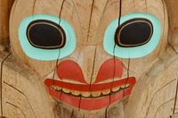 Close-up of one of the faces on a totem pole, marked by cracks in the wood.