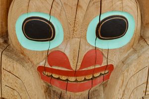 Close-up of one of the faces on a totem pole, marked by cracks in the wood.
