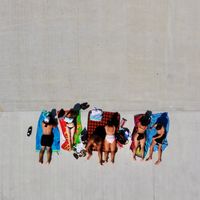 An aerial drone shot looking directly down at 3 couples sunbathing on towels on a concrete pier.