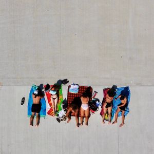 An aerial drone shot looking directly down at 3 couples sunbathing on towels on a concrete pier.
