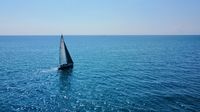 An aerial drone shot of a sailboat heading towards the horizon on a sunny day.