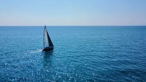 An aerial drone shot of a sailboat heading towards the horizon on a sunny day.
