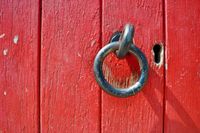 A minimalist close-up of a weathered wooden red door featuring a keyhole and a metal ring.