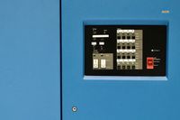 A minimalist close-up of an old mainframe computer. A single black control panel of labels and switches is surrounding by bright blue panels.