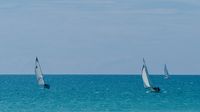 Three sailboats, at different distances, travel in the same direction on a sunny day.