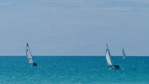 Three sailboats, at different distances, travel in the same direction on a sunny day.