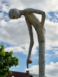 A very tall, skinny sculpture of a human leans over and is seen pointing down at the ground.