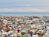 A cityscape of mid-rise buildings in every color. An overcast sky over the North Atlantic Ocean is in the background.
